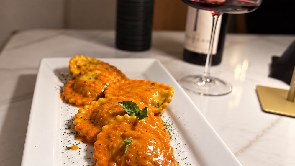 Ravioli in rose sauce on a white plate, with a glass of red wine.